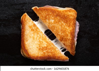 Classic cheese and ham toasted sandwich cut in half isolated on black cast iron griddle. Top view. - Powered by Shutterstock