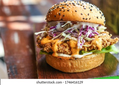 Classic cheeseburger sprinkled with sesame seeds. Fresh and tasty crispy chicken burger with melted cheese, red cabbage, lettuce and sauce on the wooden platter. Image - Powered by Shutterstock