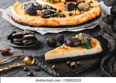 Classic Cheesecake With Caramel, Mini Oreos, Mint Leaves, And Berries On Paper Over Dark Background, Close Up View. Slice Of Cheesecake On Black Rock Plate. Delecious Sweets And Dessert