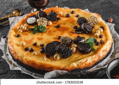 Classic Cheesecake With Caramel, Mini Oreos, Mint Leaves, And Berries On Paper Over Dark Background, Close Up View. Delecious Sweets And Dessert