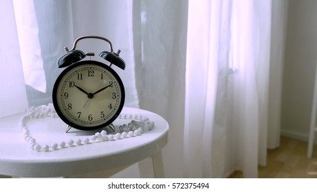 classic clock on white table in bedroom, alarm clock with pearl necklace on white background