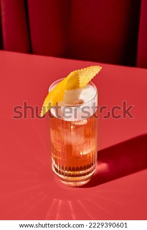 Classic cocktail whiskey sour with egg foam in highball glass on red background. Whiskey sour on coloured background in trendy style. Contemporary concept with alcohol beverage with shadow