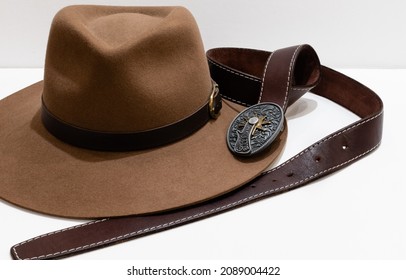 Classic Cowboy Brown Felt Hat And Leather Belt With Vintage Metal Buckle On White Background. Illustrative Editorial. Ukraine, Zhytomyr, December, 10, 2021