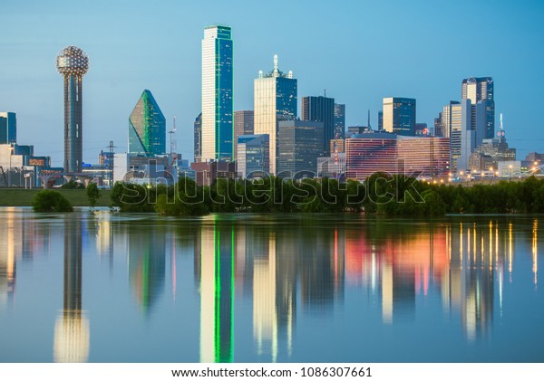 The classic Dallas, Texas skyline at dusk,\
with reflections in the Trinity\
River.