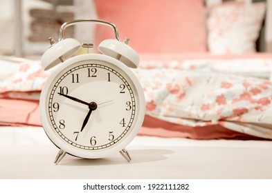 Classic design white alarm clock showing time about seven in morning on background of bed linen pink pastel shades. Happy morning concept, early rise, bedroom interior detail. Space for text.