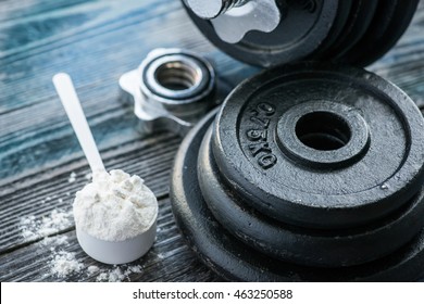 Classic dumbbell with protein powder on wooden table
