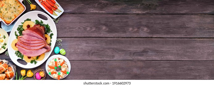 Classic Easter Ham Dinner. Overhead View Border On A Dark Wood Banner Background With Copy Space. Ham, Scalloped Potatoes, Eggs, Hot Cross Buns, Carrot Cake And Vegetables.