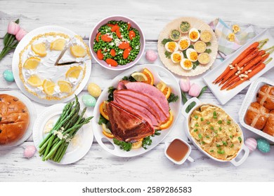 Classic Easter ham dinner. Overhead view table scene on a white wood background. Ham, scalloped potatoes, vegetable side dishes, eggs, breads and lemon cake dessert.