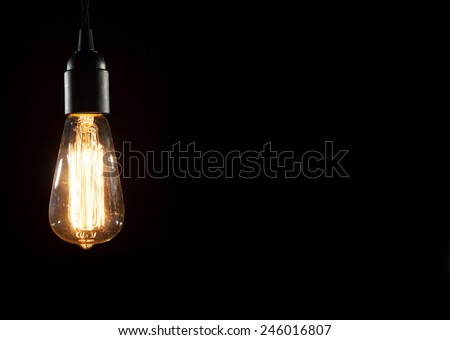 A classic Edison light bulb on black background with space for text