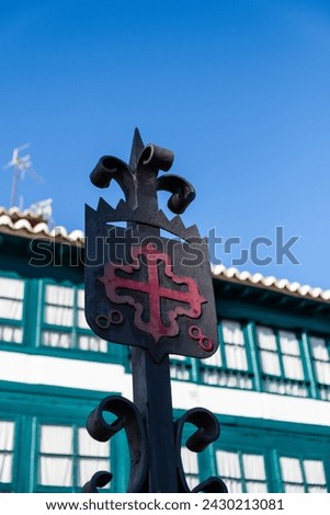 Classic Emblem of the Order of Calatrava, red Greek cross with fleur-de-lis at its ends, in the Plaza Mayor of Almagro, Ciudad Real with the typical buildings of the town bokeh in the background