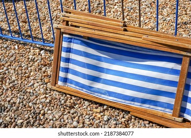 Classic English Deckchairs On Stony Beach. Traditional Blue And White Striped Deck Chairs. Vintage Wooden Beach Seats