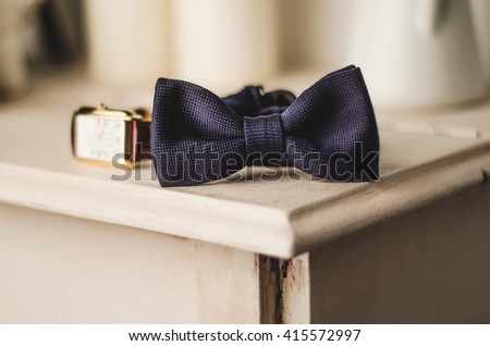Classic groom accessories: blue bow tie and watch on a wooden table. Set of men's stylish vintage clothing. Male decoration for couple. Jewelry for man. Groom's morning.
