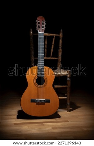 CLASSIC GUITAR AND AN OLD CHAIR ON DARK BACKGROUND ON THE STAGE IN SEVILLE, SPAIN. TYPICAL SPANISH FLAMENCO STILL LIFE IN ANDALUSIA.