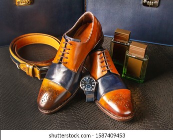 Classic handmade shoes for men and stylish men's accessories on a background of python skin. Brogues, men's watches, a trouser belt and two bottles of men's perfumes 