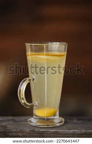 Classic herbal tea with slice of lemon and with a piece of ginger at the bottom of the glass. wooden table