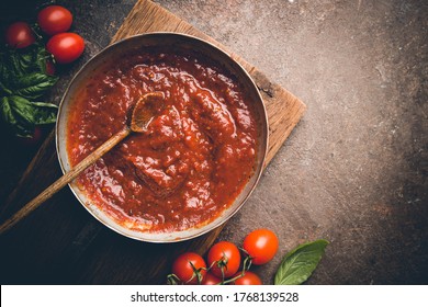 Salsa clásica italiana de tomate casera con albahaca para pasta y pizza en la sartén sobre un tablero de madera con fondo marrón, vista de arriba.