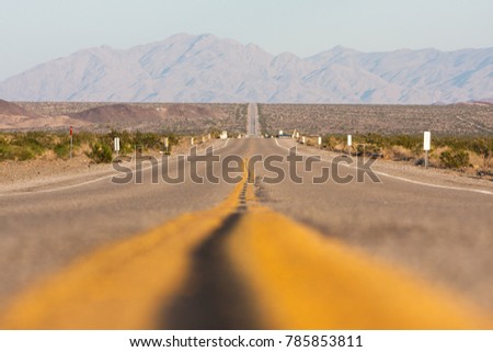 Classic horizontal panorama view of an endless straight road running through the barren scenery of the American Southwest on a beautiful day
