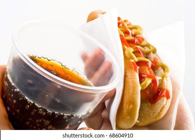 classic hot dog with mustard and ketchup in paper napkin and a glass of cola holding in hands