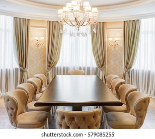 Classic Interior Of Dining Room In Brown, White, Beige Colors, With Crystal Chandelier In The Center Of Ceiling. Long Wooden Table And Many Chairs Around, Room For Big Family.