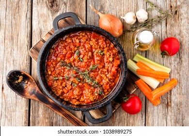 classic italian bolognese sauce stewed in stewpot with ingredients on wooden table, top view