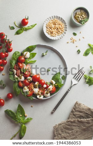 Classic italian caprese salad in grey ceramic plate with fresh tomatoes,mozzarella,basil,pine nuts,pesto and fresh oregano.Foodstyling.Top view with copy space. Stock photo © 