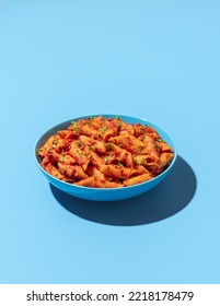 Classic italian pasta dish, penne alla arrabbiata, minimalist on a blue-colored table. Penne pasta with tomato sauce and chili on a blue plate. - Shutterstock ID 2218178479