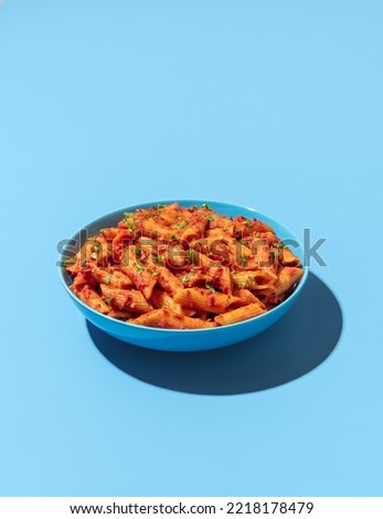 Classic italian pasta dish, penne alla arrabbiata, minimalist on a blue-colored table. Penne pasta with tomato sauce and chili on a blue plate.