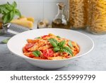 Classic italian pasta penne alla arrabiata with basil and freshly grated parmesan cheese on dark table. Penne pasta with chili sauce arrabbiata.