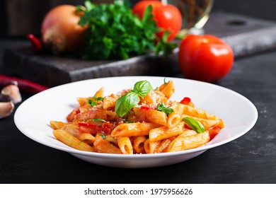 Classic italian pasta penne alla arrabiata with basil and freshly grated parmesan cheese on dark table. Penne pasta with chili sauce arrabbiata. - Shutterstock ID 1975956626