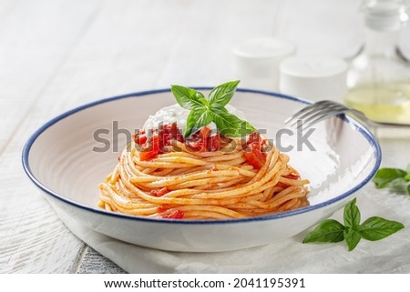 Classic italian pasta spaghetti with tomato sauce, basil and stracciatella cheese. Close-up, light background.