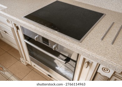 classic kitchen setup with a black induction cooktop embedded in a speckled quartz countertop, paired with a stainless steel oven, set against cream-colored ornate cabinetry