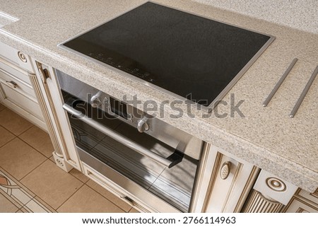 classic kitchen setup with a black induction cooktop embedded in a speckled quartz countertop, paired with a stainless steel oven, set against cream-colored ornate cabinetry