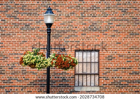 Classic light pole with hanging flower baskets against a brick wall with a bar covered window
