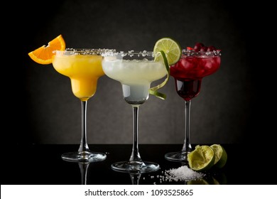 Classic Lime Margarita, Orange Margarita And Cherry Margarita Cocktail Mix In Salt Rimmed Glasses Garnished With Slices Of Lime, Orange And Cherries