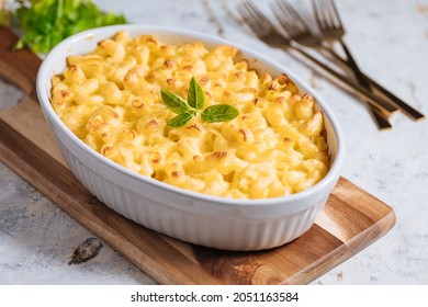 Classic mac and cheese baked in oven with basil on top on a rustic wooden board