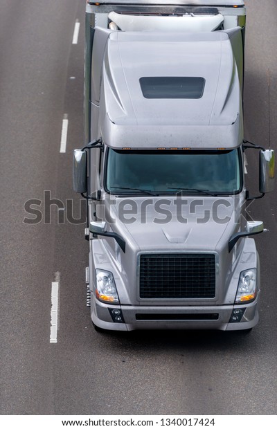 Classic modern design stylish gray big rig bonnet\
long haul semi truck transporting frozen and chilled cargo in full\
size refrigerated semi trailer moving on wide multiline divided\
highway road