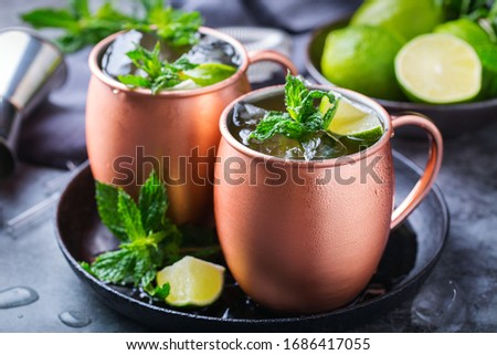 Classic Moscow mule cocktail with green lime, mint, ice in a copper mug on a black table.