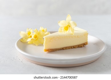 Classic New York Cheesecake With Fresh Vanilla Flower On A White Concrete Background, Side View. A Piece Of Vanilla Cheesecake On A White Plate. Confectionery Menu, Recipe. Close Up