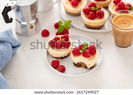 Classic New York cheesecakes in individual cups topped with fresh raspberry served with coffee with a bite taken