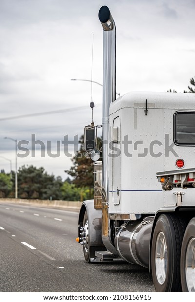 Classic old style bonnet white semi truck with\
additional side lights and tall chrome exhaust pipes transporting\
empty flat bed semi trailer running on the highway road to\
warehouse for the next\
load