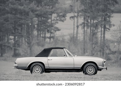 Classic oldtimer vintage luxury sports cabrio car of the 1960s - 1970s on a country road in a forest.