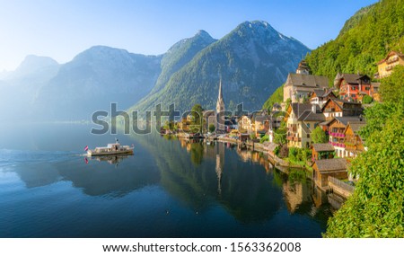 Classic panoramic view of famous old town Hallstatt and alpine deep blue lake with tourist ship in scenic golden morning light on a beautiful sunny day at sunrise in summer, Salzkammergut, Austria