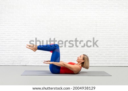 Classic pilates, the hundred drill. Caucasian woman in sportswear lying on her back on a mat and does workout in loft fitness studio indoor, side view
