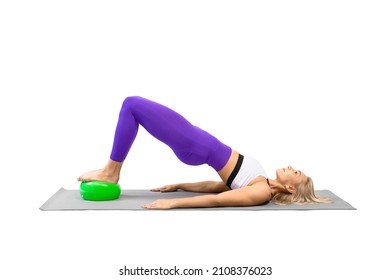Classic pilates with props. Athletic woman practice shoulder bridge with a small fit ball under her feet, isolated on white.