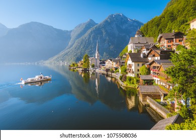 Classic postcard view of famous Hallstatt lakeside town with traditional ship in beautiful morning light at sunrise in summer, Salzkammergut, Austria