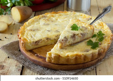A classic quiche Lorraine pie with potatoes, meat and cheese on a wooden table. Space for your text.