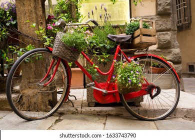 Classic Red Bike Adorned With Flowers, Basket And Wine Crate In Cortona, A Hill Town In The Tuscany Region Of Italy