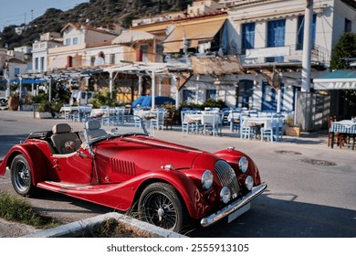 A classic red convertible car parked on a sunny street in a picturesque coastal town, with traditional buildings and outdoor seating in the background. - Powered by Shutterstock