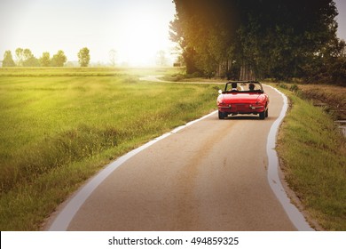 Classic red convertible car traveling in the countryside at sunset