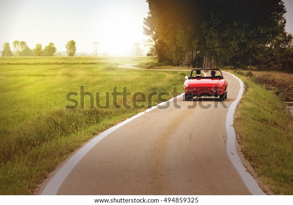 Classic red convertible car traveling in the\
countryside at sunset